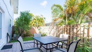 A patio with a table and chairs, surrounded by a wooden fence and palm trees.