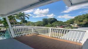 A wooden deck with white railings, a clear view of the surrounding greenery, and a partly cloudy sky. - Short Walk to Wilton Drive! Apt5 (Wilton Manors)