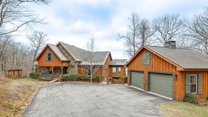 A large wooden house with a stone foundation, two garage doors, and a spacious driveway.