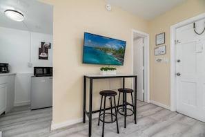 A modern kitchen with a refrigerator, microwave, and coffee maker. There is a small table with two stools and a painting of a beach scene.
