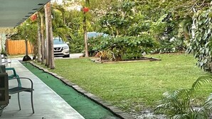 Un espace extérieur abrité, doté d’une pelouse artificielle verte, avec une voiture garée au fond et diverses plantes et arbres.