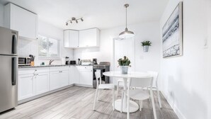 A modern kitchen with white cabinets, a stainless steel refrigerator, a built-in oven, and a dining area with a round table and chairs. - Comfy Condos @ Middle River - #1 (Fort Lauderdale)