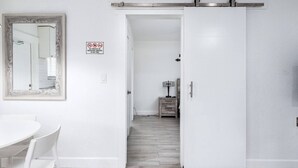 Une pièce blanche avec une porte coulissante, un miroir, une petite table avec une lampe et un panneau indiquant qu'il est interdit de fumer.