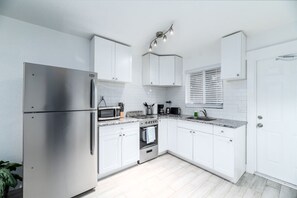 Uma cozinha moderna com armários brancos, eletrodomésticos de aço inoxidável e bancada com pia e diversos utensílios.
