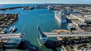 Un paysage urbain côtier avec un grand navire de croisière amarré dans un port, un pont et une marina remplie de bateaux.