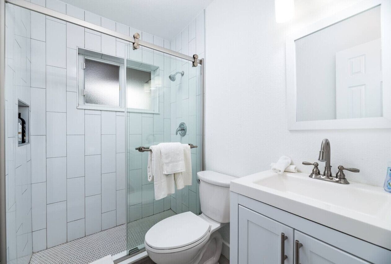 A bathroom with a glass shower enclosure, a white toilet, a sink with a mirror, and a towel rack.