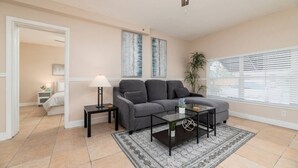 A living room with a gray sofa, a coffee table, a lamp, and a large window with blinds.