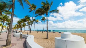 A beach with palm trees, a curved white structure, and a clear blue sky.