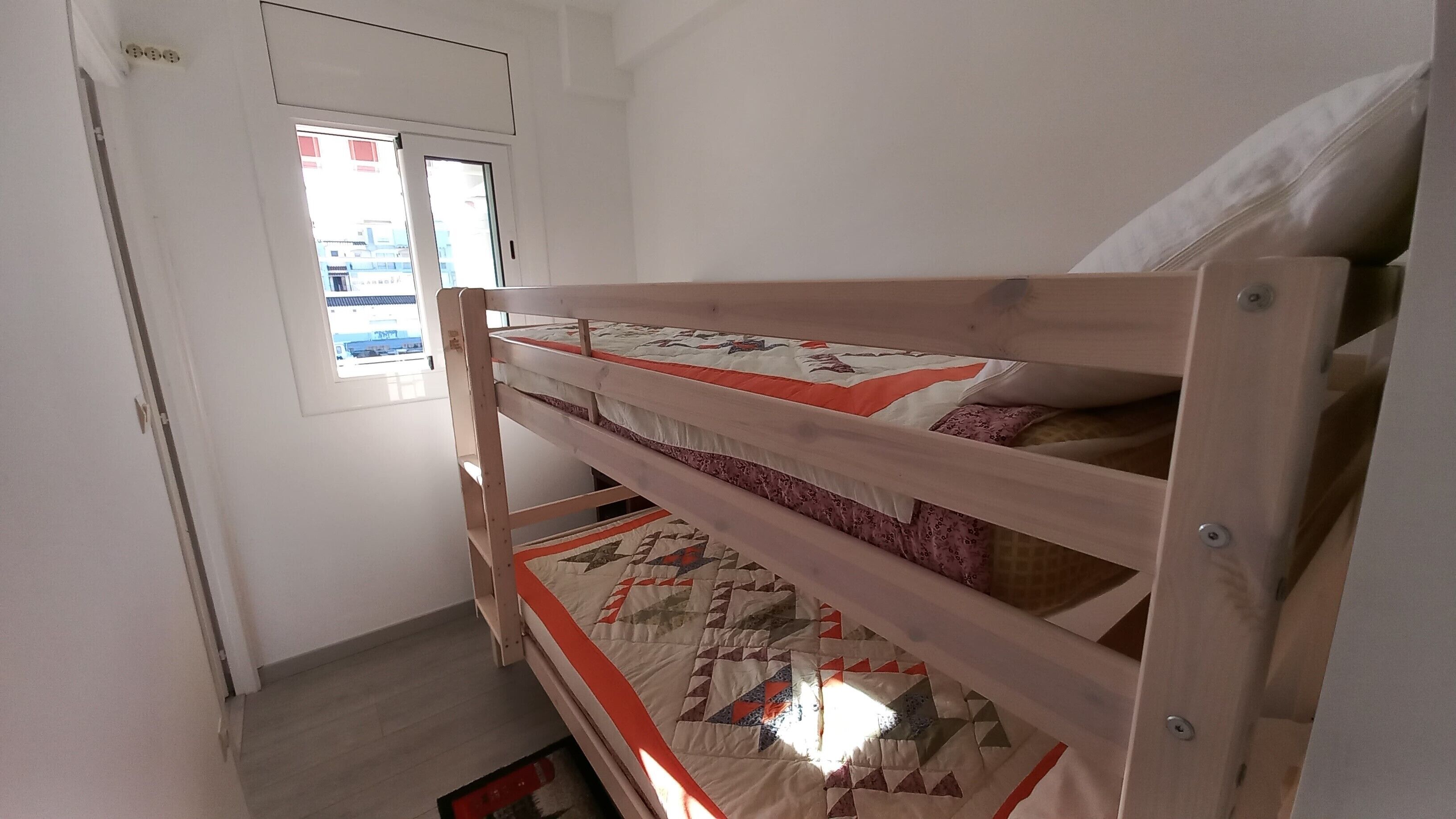 Une petite pièce étroite, avec un lit superposé, une fenêtre et une porte.