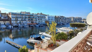 A marina with multiple boats docked, a row of residential buildings, and potted plants on a balcony.