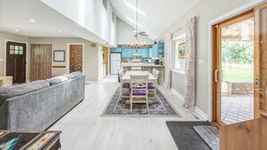 Un vaste espace de vie comprenant un canapé, une table à manger avec des chaises, une cuisine à l’arrière-plan et une grande porte-fenêtre coulissante donnant sur un espace extérieur.
