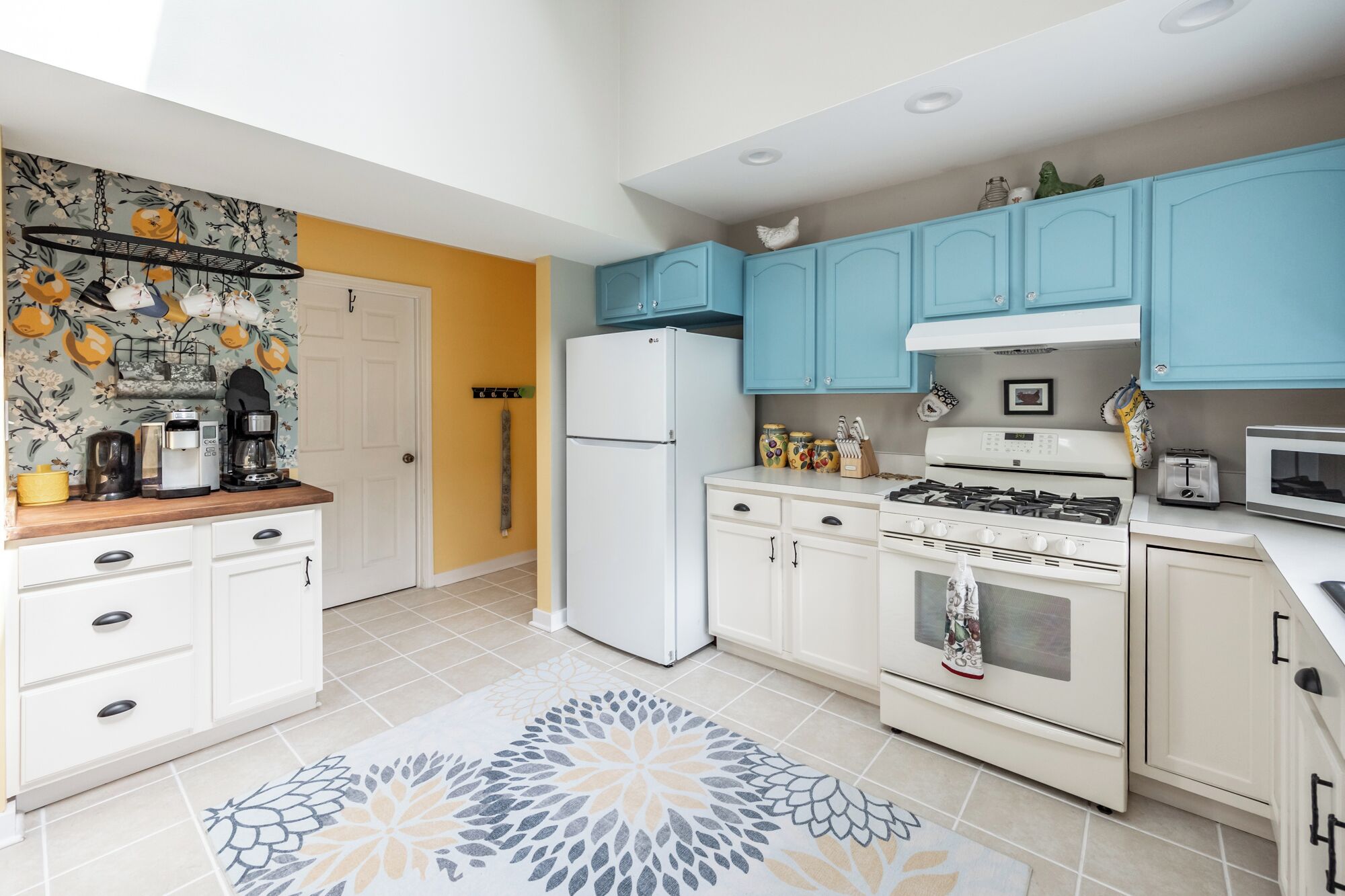 A modern kitchen with white cabinets, a blue upper cabinet, a white refrigerator, a stove, and a microwave.