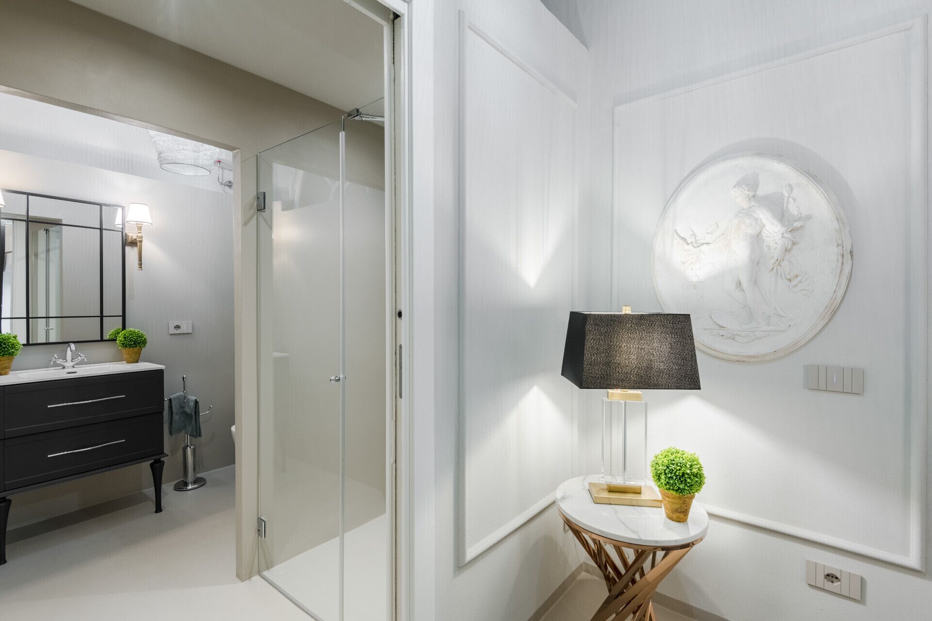 Een moderne badkamer met een glazen douchecabine, een zwart wastafelmeubel en een rond wandsculptuur.
