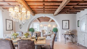 A dining area with a wooden ceiling, chandeliers, and a view through an arched doorway to another room. - Villa Lina, Luxury Farmhouse with Pool and Amazing View close to Lucca Town Centre (San Concordio di Moriano)