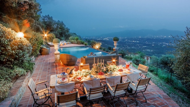 A dining area with a pool and a view of the city at dusk. - Villa Lina, Luxury Farmhouse with Pool and Amazing View close to Lucca Town Centre (San Concordio di Moriano)