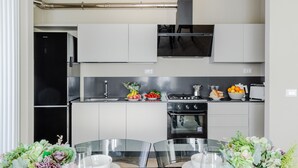 Una cocina moderna con armarios blancos, un refrigerador negro, una estufa y un lavamanos. Hay una mesa de comedor con sillas y un jarrón de flores.