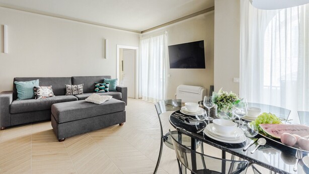 Una sala de estar moderna con un sofá gris, una mesa de comedor de cristal con platos, vasos y sandía.