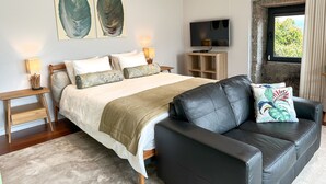 A modern bedroom with a large bed, a black leather sofa, a TV, and artwork on the wall. - Villa Isobel (Vila Verde)