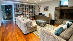 A spacious living room with a wooden floor, two large wicker sofas, a bookshelf, a fireplace, and a television. - Villa Isobel (Vila Verde)