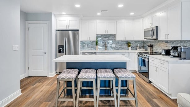 A modern kitchen with white cabinets, a stainless steel refrigerator, a built-in microwave, and a large island with bar stools. - Conveniently Located Contemporary 6 Bed/6 Bath 15 Min to Downtown (Metairie)