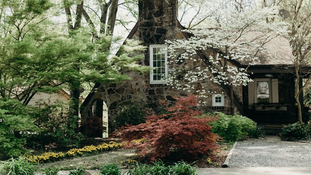 A stone house with a chimney, surrounded by a garden with various plants and flowers. - NEW! Off to the races: Stay at the spacious Woodlawn Tudor, close to Oaklawn! (Hot Springs)