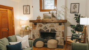A cozy living room with a stone fireplace, green sofas, a wooden coffee table, and a ceiling fan. - NEW! Off to the races: Stay at the spacious Woodlawn Tudor, close to Oaklawn! (Hot Springs)
