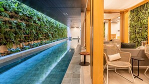 Een binnenzwembad met een groenbeplantingswand, rieten meubels en een betegelde vloer.