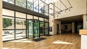 Een ruime lobby met een houten vloer, grote glazen deuren en een modern plafondontwerp.
