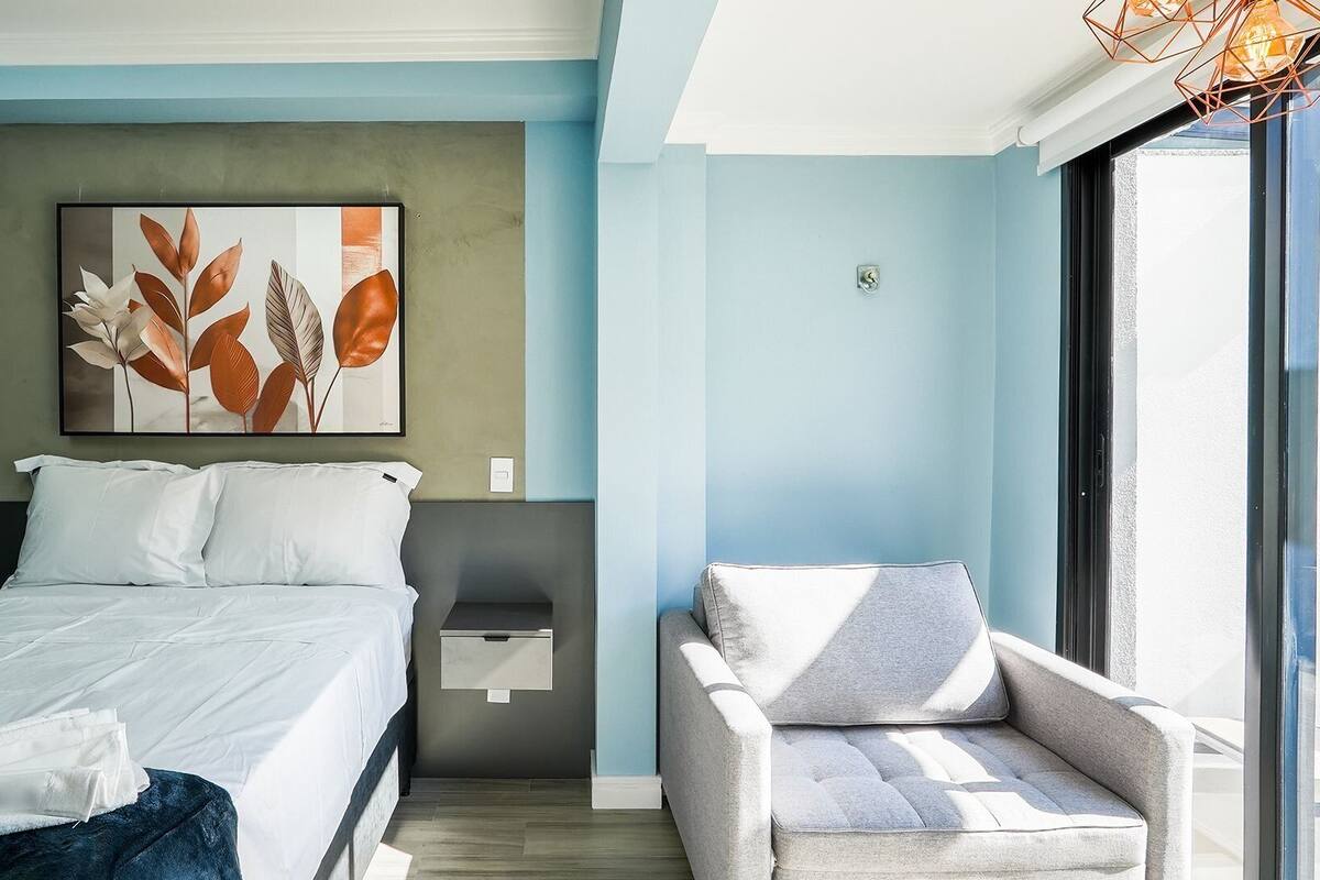 Une chambre moderne avec un lit, une table de chevet, une chaise et une grande fenêtre.