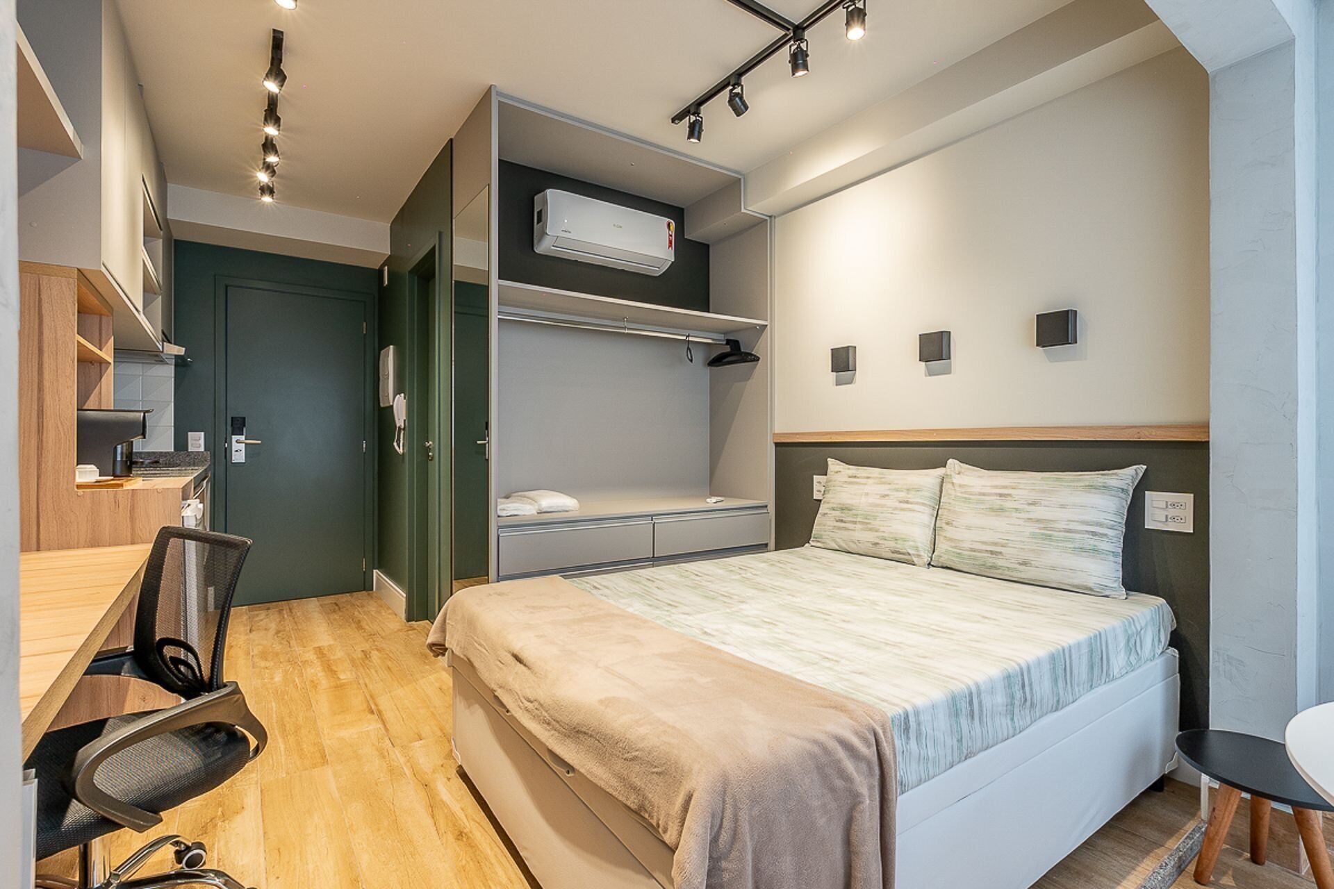 Een compacte hotelkamer met een stapelbed, een bureau met stoel, een kleine kitchenette en een nachtkastje.