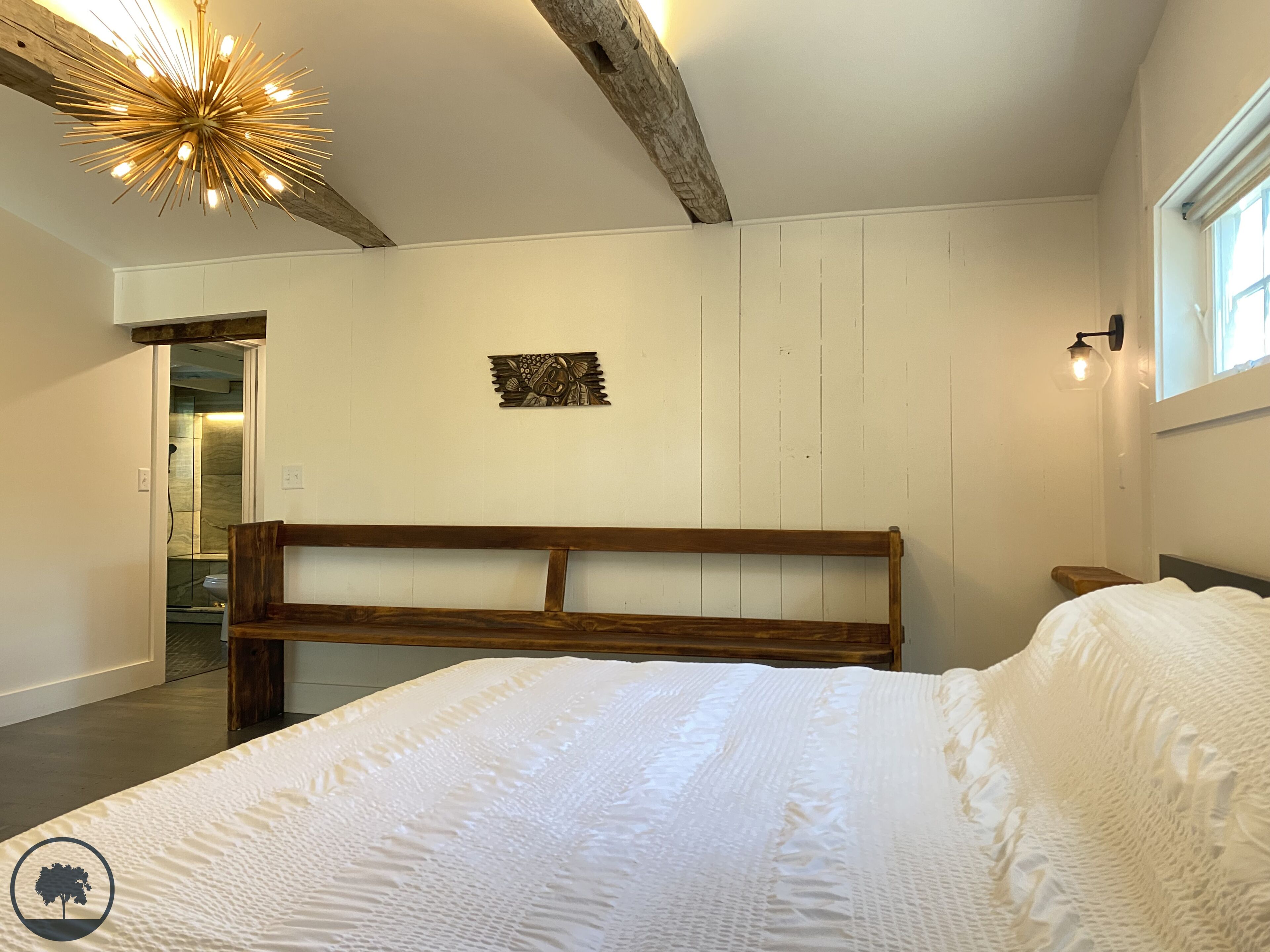 Une chambre à coucher avec une tête de lit en bois, un grand lit, un luminaire fixé au mur et une petite table.