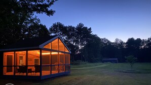 Une cabane moderne en bois, dotée de grandes fenêtres en verre, d’un coin repas et d’un espace extérieur bien visible.