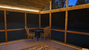 Un espace extérieur abrité, doté d’une table et de chaises, de grandes fenêtres et d’un tapis à motifs.
