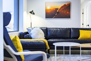 A modern living room with a black leather sofa, a white coffee table, and a large painting of a sunset on the wall.