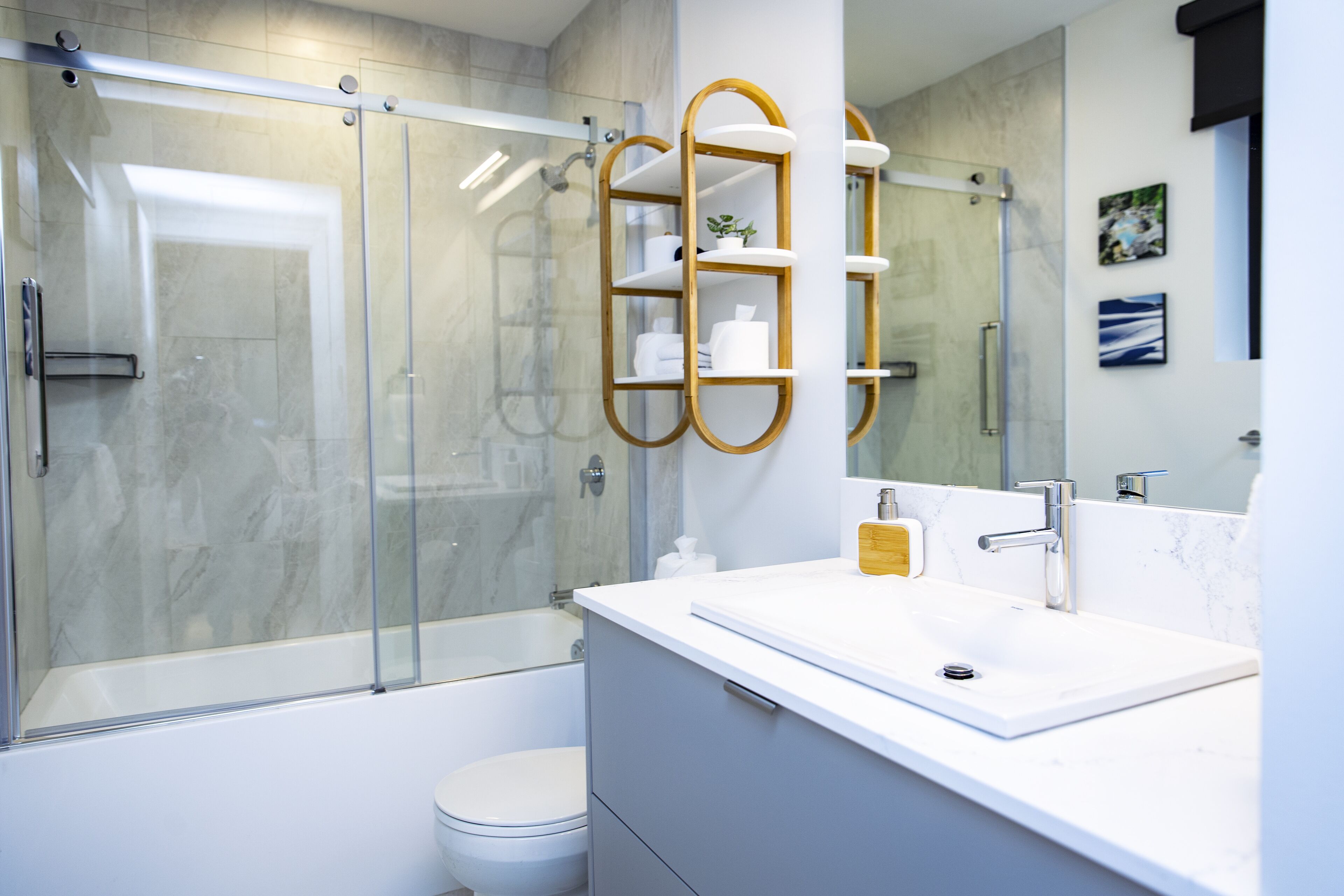 Un baño moderno con ducha de vidrio, un lavamanos blanco y un dispensador de jabón dorado, y un inodoro.