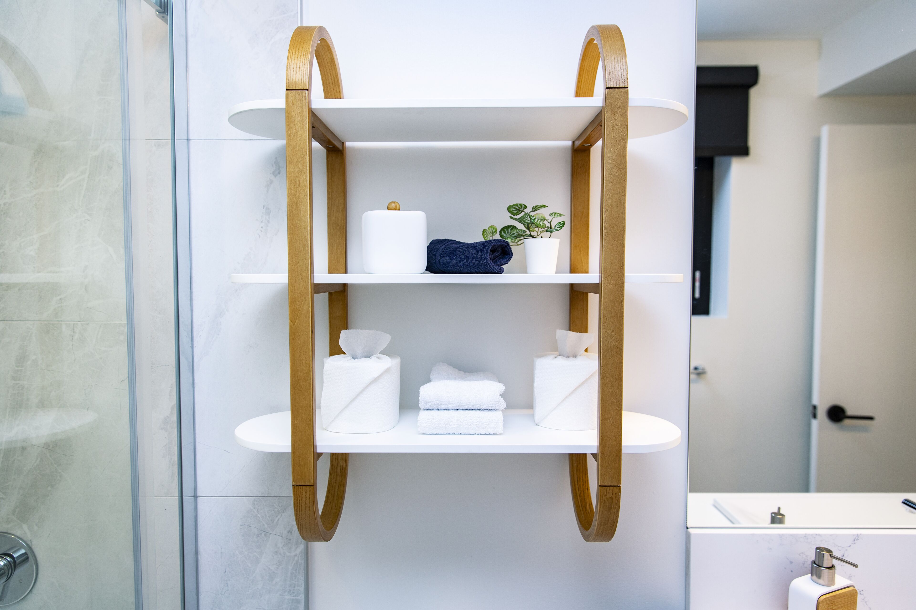 A bathroom with a wooden shelf holding toiletries, a white sink, and a mirror.