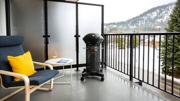 A balcony with a blue chair, a small table with a glass, and a grill.