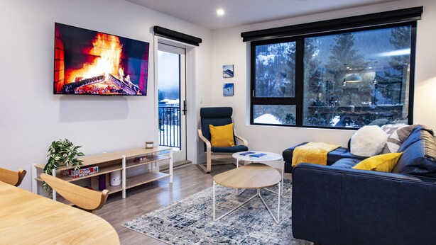 A modern living room with a fireplace, a sofa, a chair, a coffee table, and a TV mounted on the wall. - Separate Reality By Revelstoke Vacations (Revelstoke)