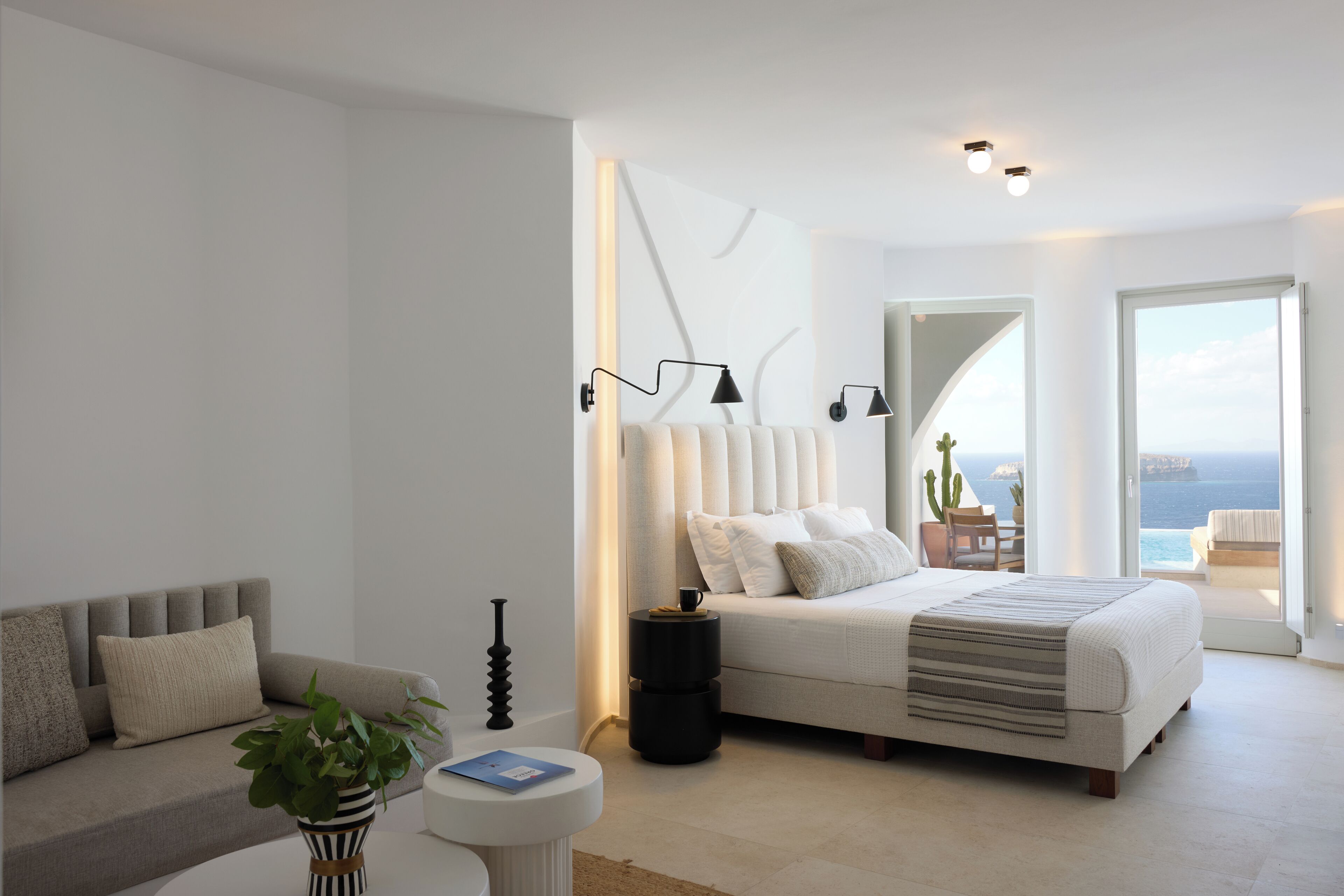 A modern bedroom with a large bed, a sofa, a small table, and a potted plant.