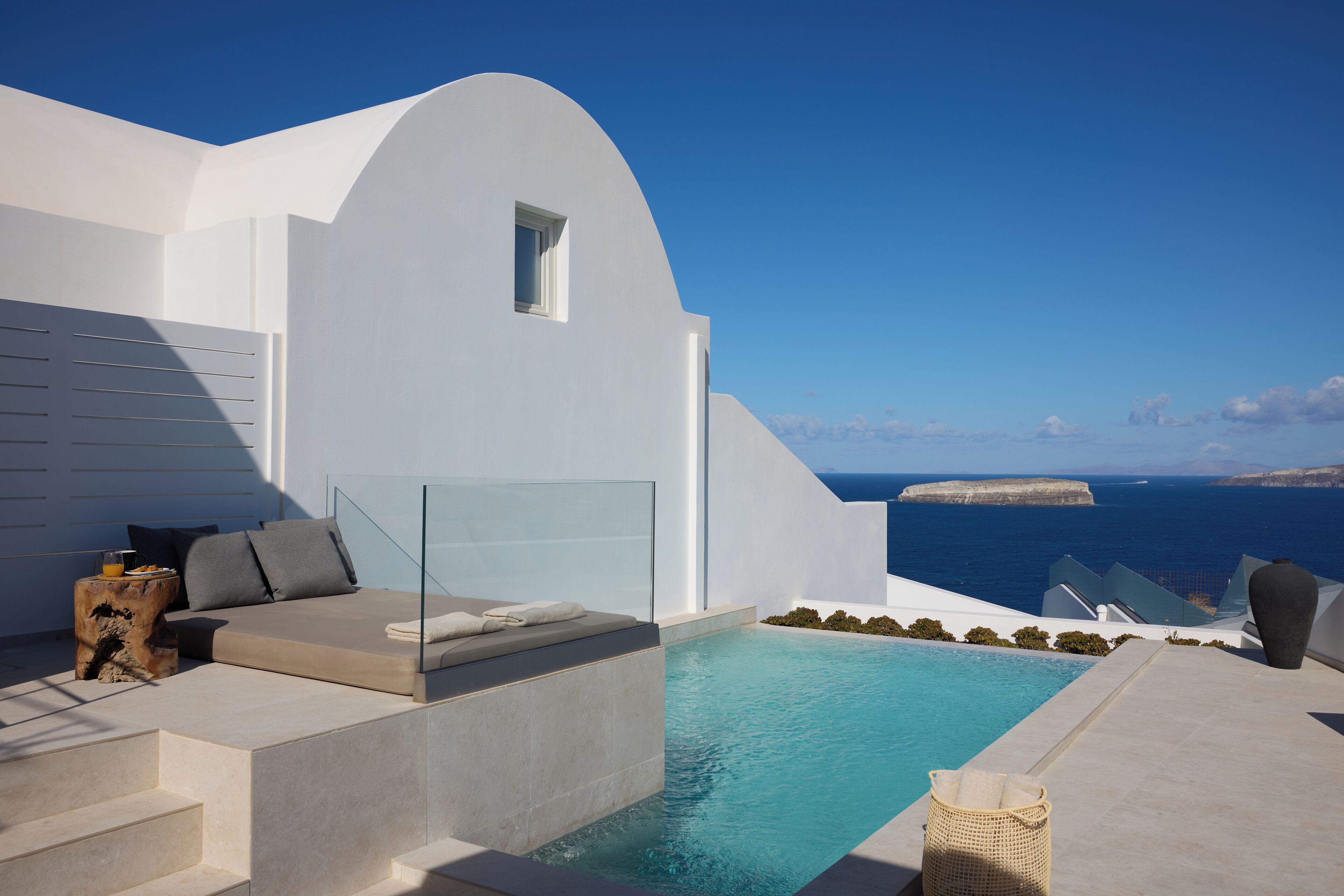 Ein moderner Poolbereich im Freien mit Glasbrüstung, einer Lounge mit Kissen und Blick aufs Meer.