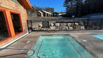 A wooden deck with a hot tub, a fenced area, and a building with a red door.