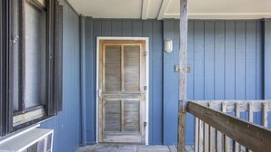 A porch with a wooden railing, a door with shutters, and a small step leading to the entrance. - Shore Beats Work - Oceanfront New Balcony 3rd Flr (North Topsail Beach)