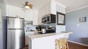 A modern kitchen with white cabinets, stainless steel appliances, a central island with stools, and a ceiling fan. - Shore Beats Work - Oceanfront New Balcony 3rd Flr (North Topsail Beach)
