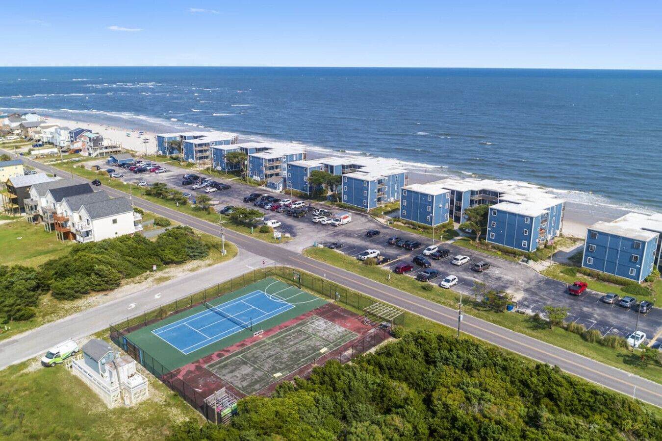 A coastal residential area with beachfront properties, a tennis court, and a parking lot.