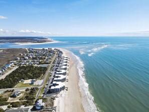 An aerial view of a coastal resort with rows of beachside villas, a sandy beach, and the ocean.