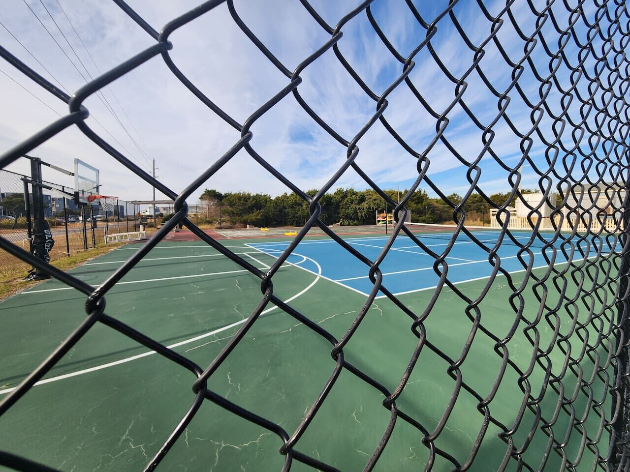 A chain-link fence surrounding a basketball court with a blue surface and white lines.