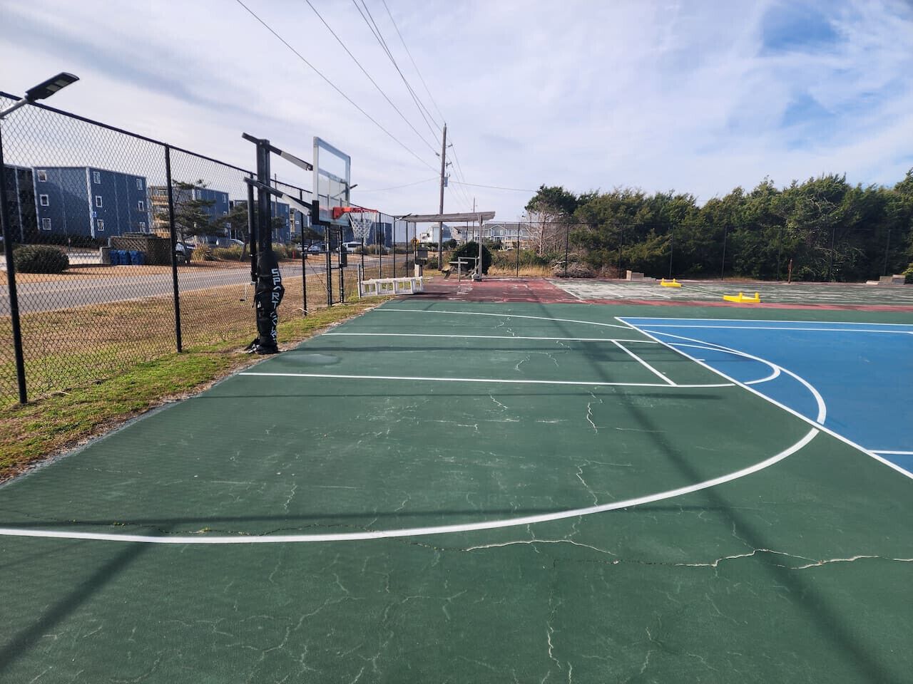 Een buitenbasketballveld met een groene ondergrond, omgeven door een hek van gaas.