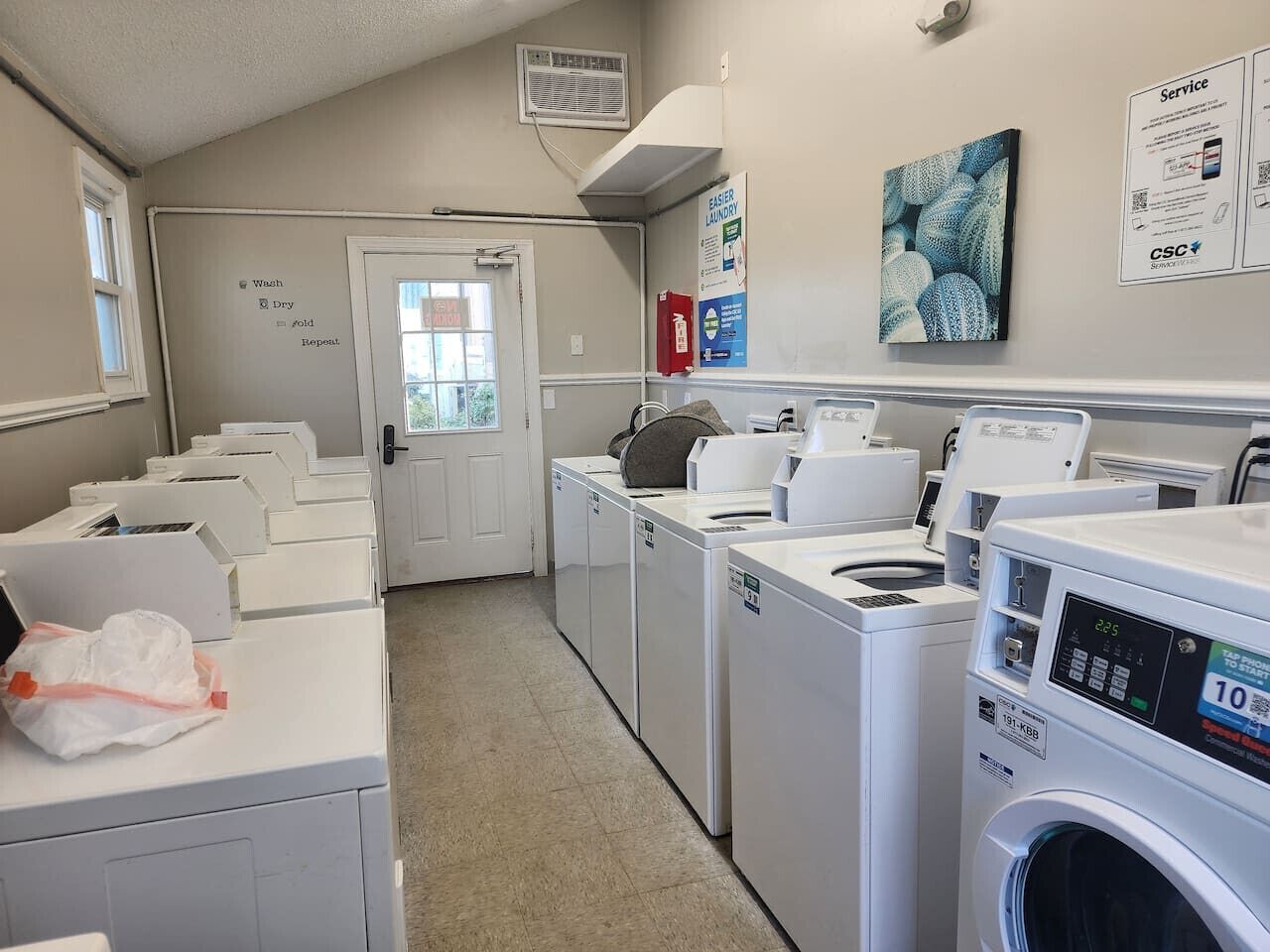 A laundry facility with multiple washing machines and dryers, a fire extinguisher, and a door leading to another room.