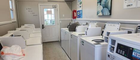A laundry facility with multiple washing machines and dryers, a fire extinguisher, and a door leading to another room.