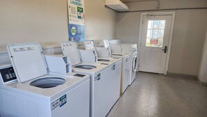 A laundry facility with multiple washing machines, a sign promoting easier laundry, and a door with a window. - Shore To Please, 1st Floor Oceanfront Condo (North Topsail Beach)